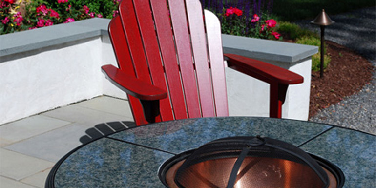 Close up of a outdoor firepit with patio chair with gardens around the patio.