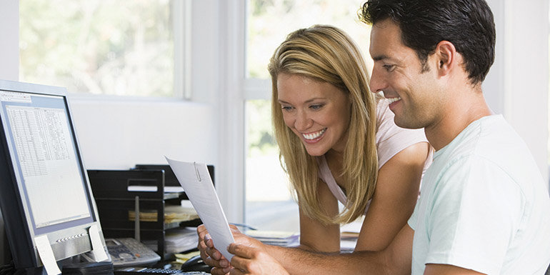 Couples In Home Office With Computer And Paperwork Smiling