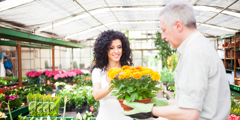 Portrait of a greenhouse worker giving a plant to a customer