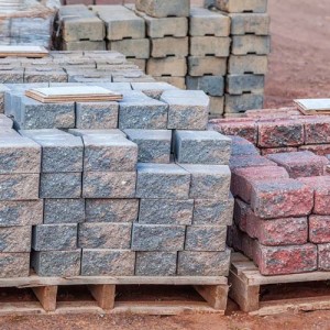 Stacks of various colored concrete pavers (paving stone) or patio blocks organized on wooden pallets and for sale in a retail setting such as a garden center or building supply.