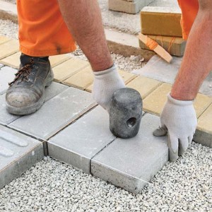 Construction site worker installing concrete brick pavement using hammer