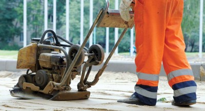 Worker in overalls controls plate compactor