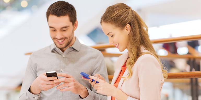 sale, consumerism, technology and people concept - happy young couple with shopping bags and smartphones in mall