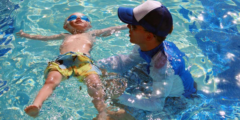 Young child learning water safety in pool with an instructor