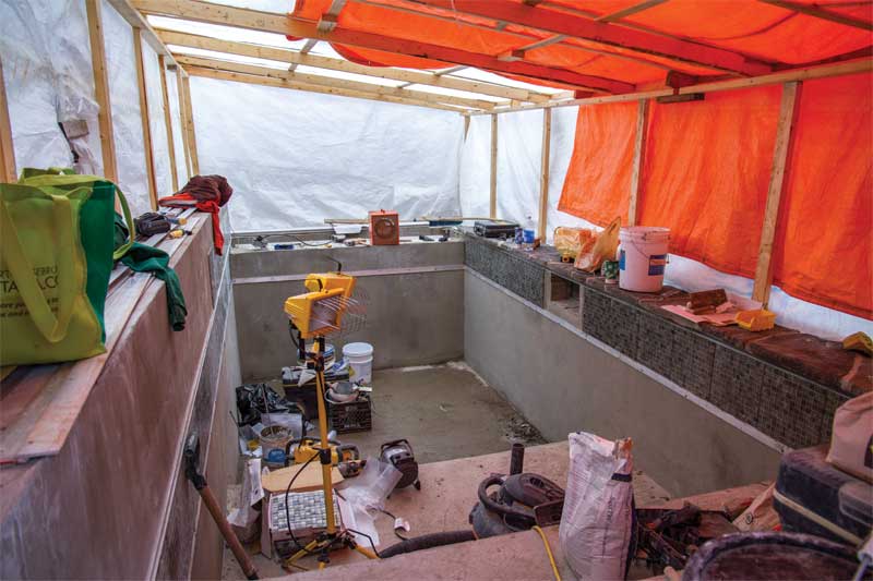 Working in comfort under a temporary construction tent, workers install glass mosaic tiles on this 2.4- x 4.8-m (8-x 16-ft) concrete pool.