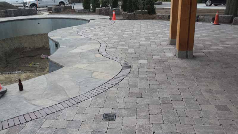 A brick border separates the flagstone pool deck from the adjacent outdoor living space.