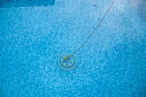 The technician drops the hydrophone into the pool and listens for the sound of leaks from inside the pool shell with an amplifier.