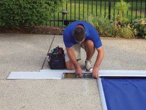 A service technician squatting by the pool, operating on a pool cover.