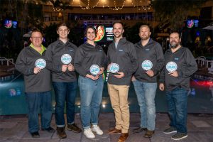 Group of Pleatco Pool Tech Search winners holding awards by a pool at night.