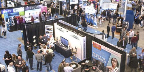 Overhead view of a bustling trade show floor with various exhibitors and attendees networking around booths and displays.