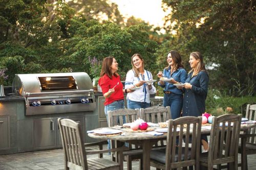 group of women gathered around a table with a grilling station behind them