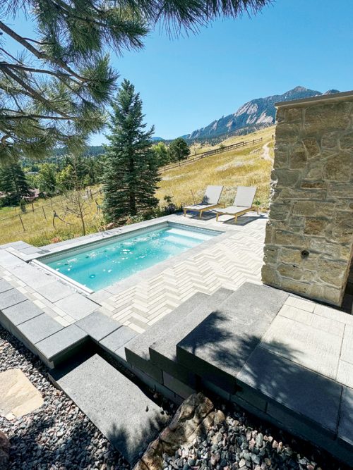 A crystal-clear pool with bubbling water next to a patio featuring striped chairs and a small table.