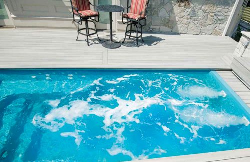 A crystal-clear pool with bubbling water next to a patio featuring striped chairs and a small table.