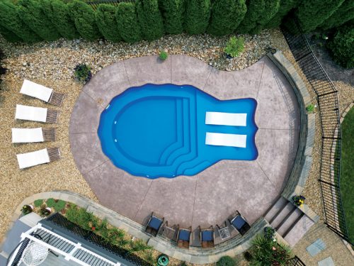 Aerial view of a curved swimming pool surrounded by lounge chairs and decorative landscaping.