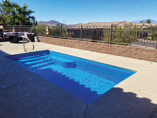 A serene backyard featuring a blue pool, steps, and a view of mountains and houses in the background.