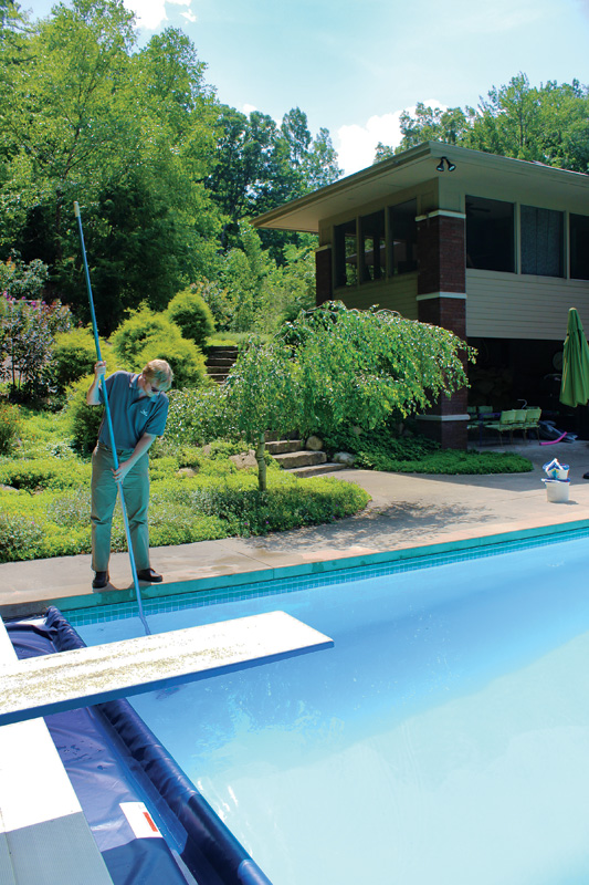 A man stands beside a pool, showcasing reflections on the water's surface and the surrounding landscape's vibrant colors.