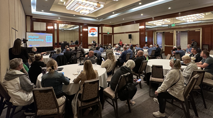 Conference room with attendees seated at round tables watching a "Digital Marketing" presentation. IPSSA logo is visible.