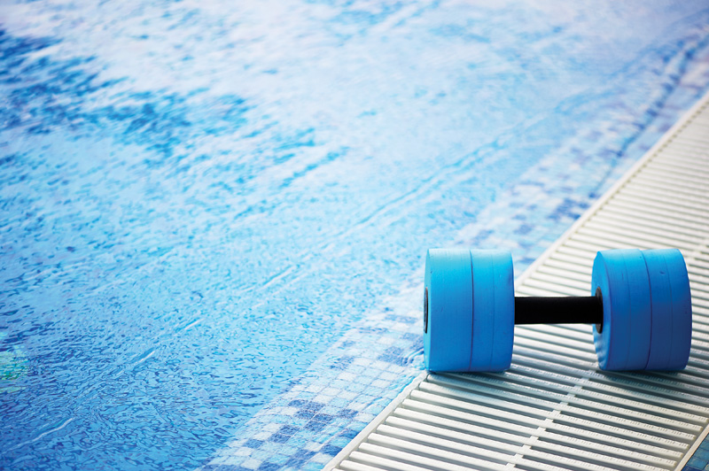 Blue foam water dumbbell resting on the edge of a swimming pool, used for aquatic exercise and water aerobics.