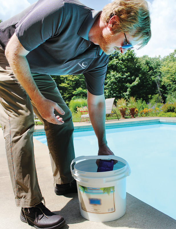 Pool maintenance worker placing a purple package into a white bucket near a swimming pool